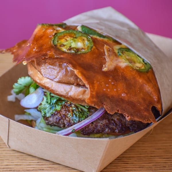 Sideburns' burger with melted cheese, jalapeños, red onion, and cilantro in a paper tray.