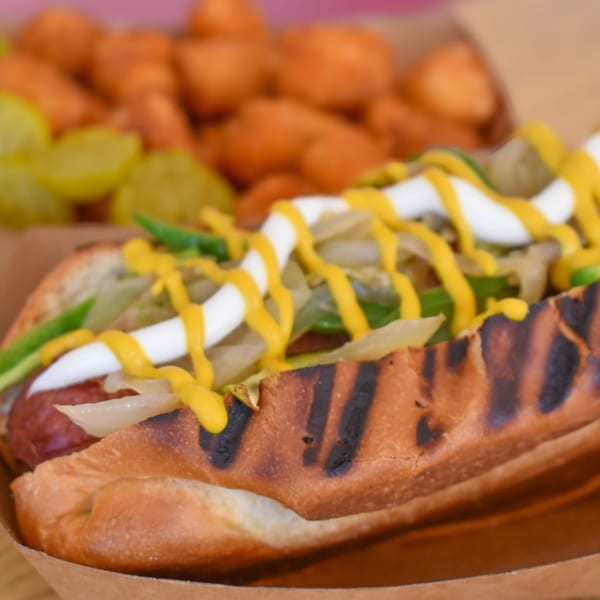 A Sideburns hot dog with mustard, mayonnaise, onions, and green peppers, with tater tots and pickles.