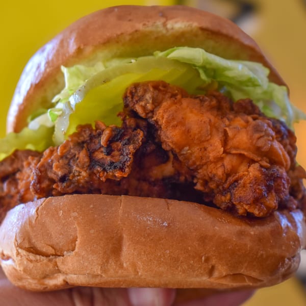 Close-up of a Sideburns fried chicken sandwich with lettuce on a brioche bun.